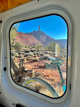RV rental view: a mountain bike through the window, overlooking a vast desert and a striking rock formation. Van life adventure.