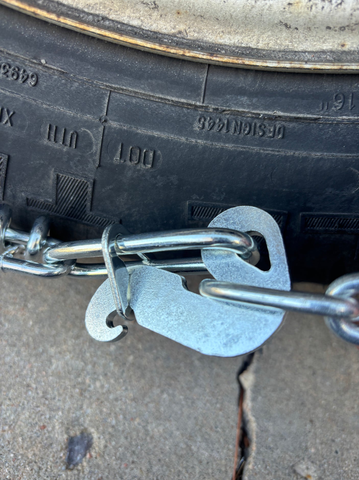 Close-up of shiny metal snow chains attached to a dark rubber tire, likely on an RV rental, for enhanced traction.
