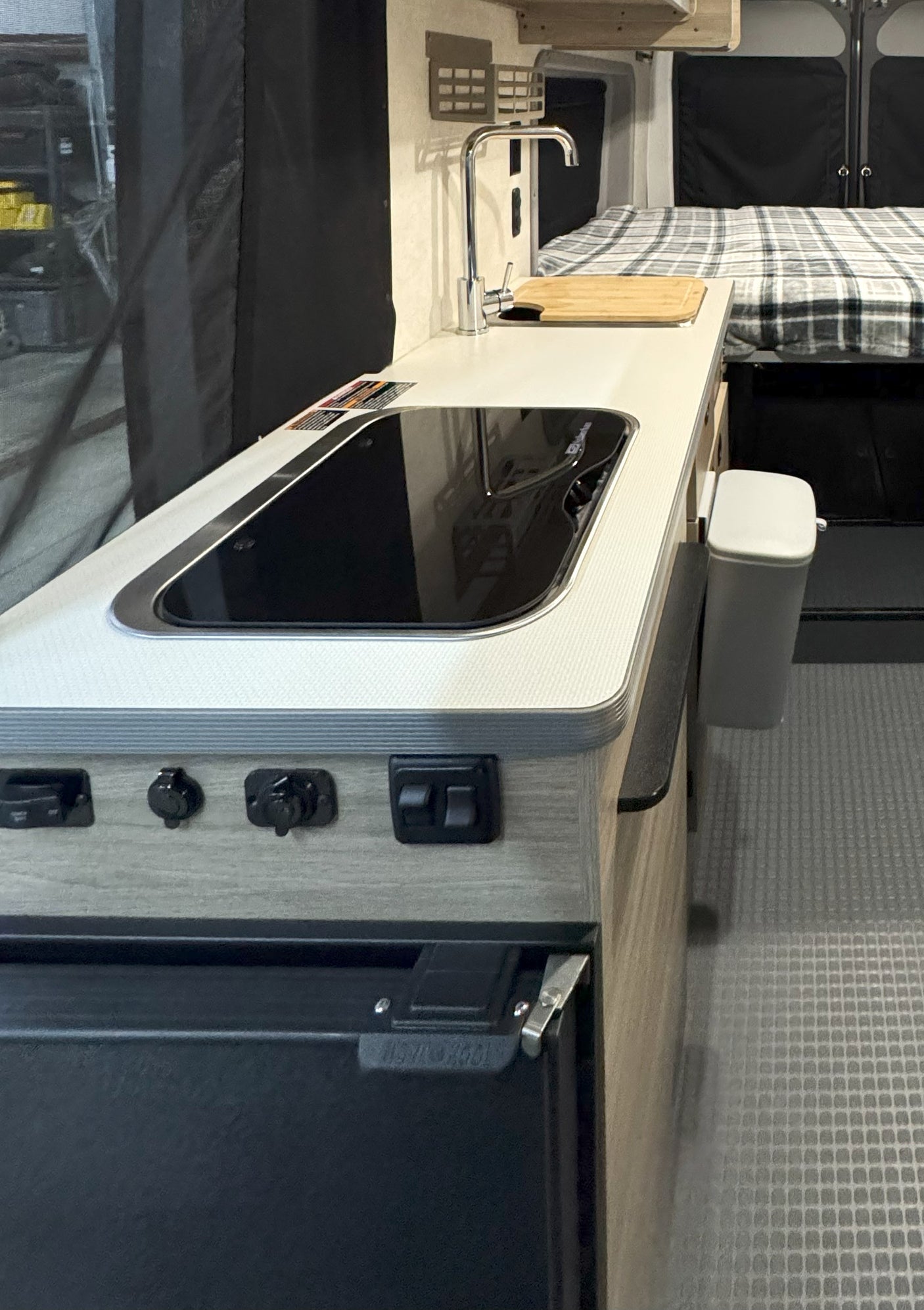 Modern RV rental interior: kitchenette with sink, induction cooktop, and sleeping quarters in the background.