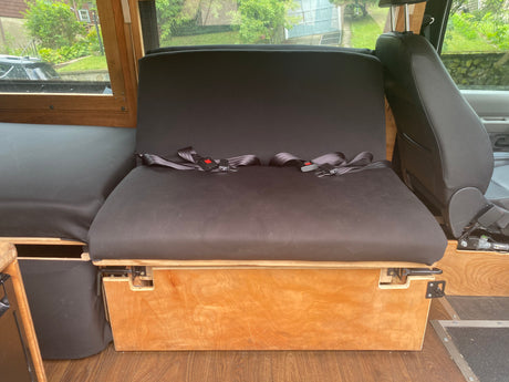 Inside an RV rental: A sturdy wooden bench with black cushions & seatbelts provides comfortable passenger seating.