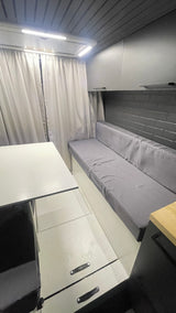 RV rental interior: compact living space with white table, gray bench, floor storage, and bright LED lighting. Ideal for travel.