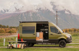 Scenic rv rental: A green camper van with open door & picnic table, set against snow-capped mountains.