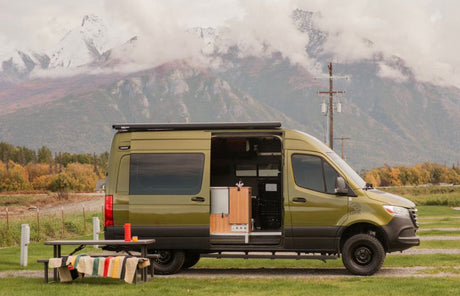 Scenic rv rental: A green camper van with open door & picnic table, set against snow-capped mountains.