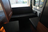 Experience comfort in this RV rental's lounge. Features black upholstered bench seating, wood panels, and rear windows.