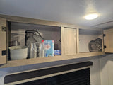 Inside an RV rental cabinet: organized kitchenware like bowls, cups, cutlery, and a neatly rolled towel.