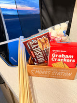 S'mores station with Hershey's, graham crackers, marshmallows, and roasting sticks, perfect for an rv rental with a sunset view.