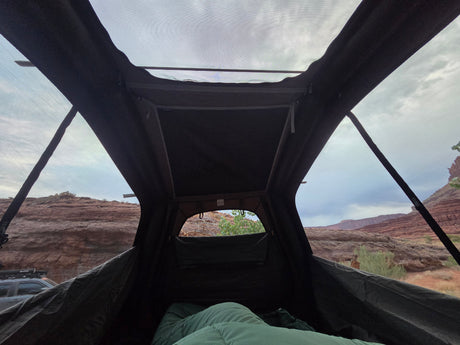 Relaxing inside a rooftop tent, looking out at a stunning red rock desert landscape. Ideal for an RV rental camping trip.