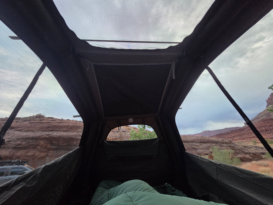 Relaxing inside a rooftop tent, looking out at a stunning red rock desert landscape. Ideal for an RV rental camping trip.