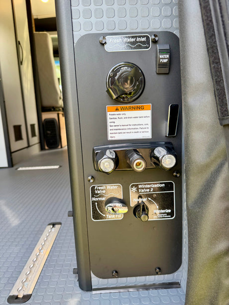 This RV rental's water system panel shows the fresh water inlet, pump switch, and winterization valves for tank maintenance.