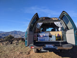 Rear of a converted SUV/van set up for rv rental car camping, showcasing organized gear, curtains, and mountain views.