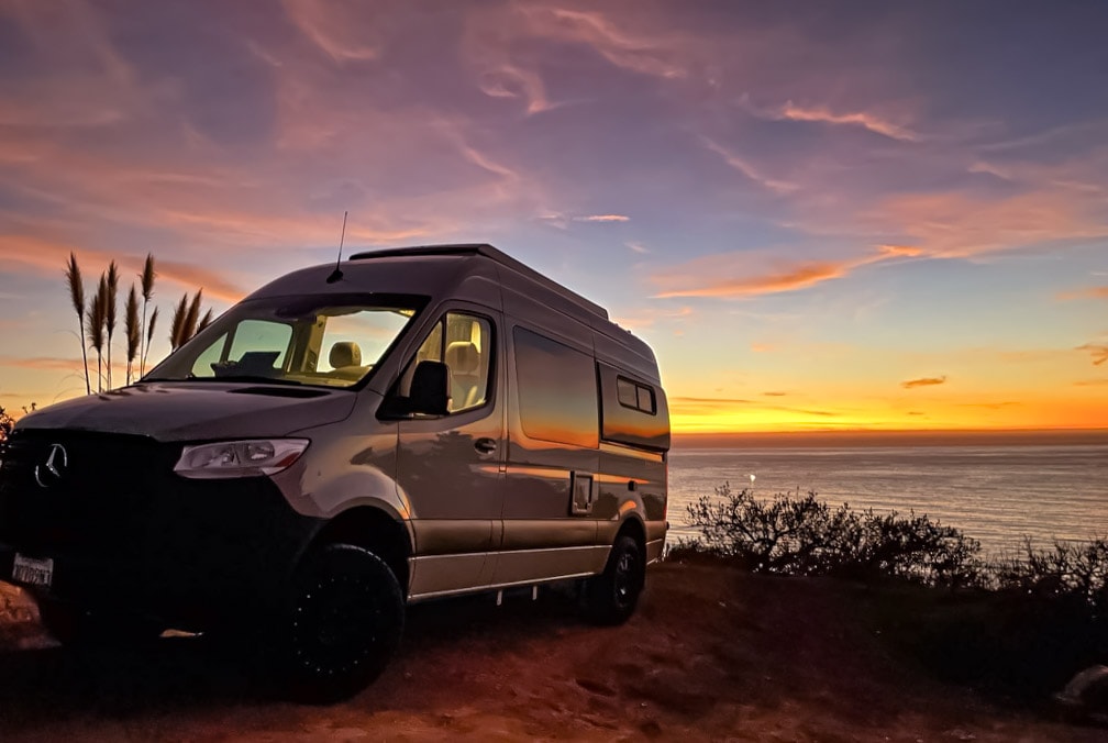 A sleek RV rental is perfectly positioned on a cliff overlooking the ocean at a vibrant sunset. — photo 13
