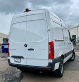 Rear view of a white Mercedes-Benz Sprinter van, suitable for an RV rental, parked on asphalt under cloudy skies.