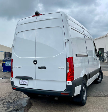 Rear view of a white Mercedes-Benz Sprinter van, suitable for an RV rental, parked on asphalt under cloudy skies.