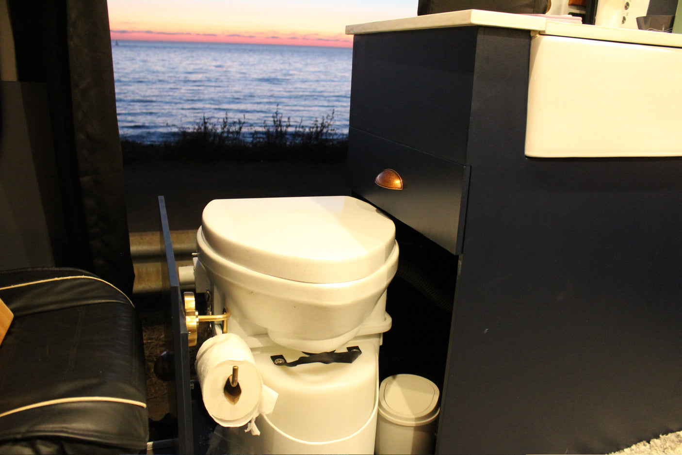 RV rental: Camper van interior with a composting toilet, sink, and ocean sunset view. Perfect for travel.