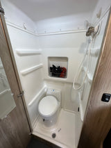 Clean and compact RV rental bathroom, featuring a white shower unit, toilet, and built-in storage.