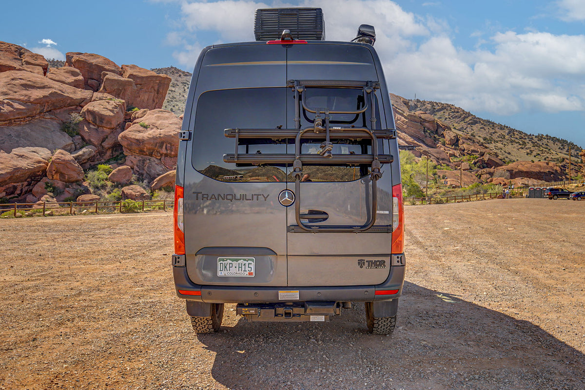 Rear of a gray rv rental camper van with a bike rack, parked in a scenic red rock mountain landscape under a blue sky. — photo 14