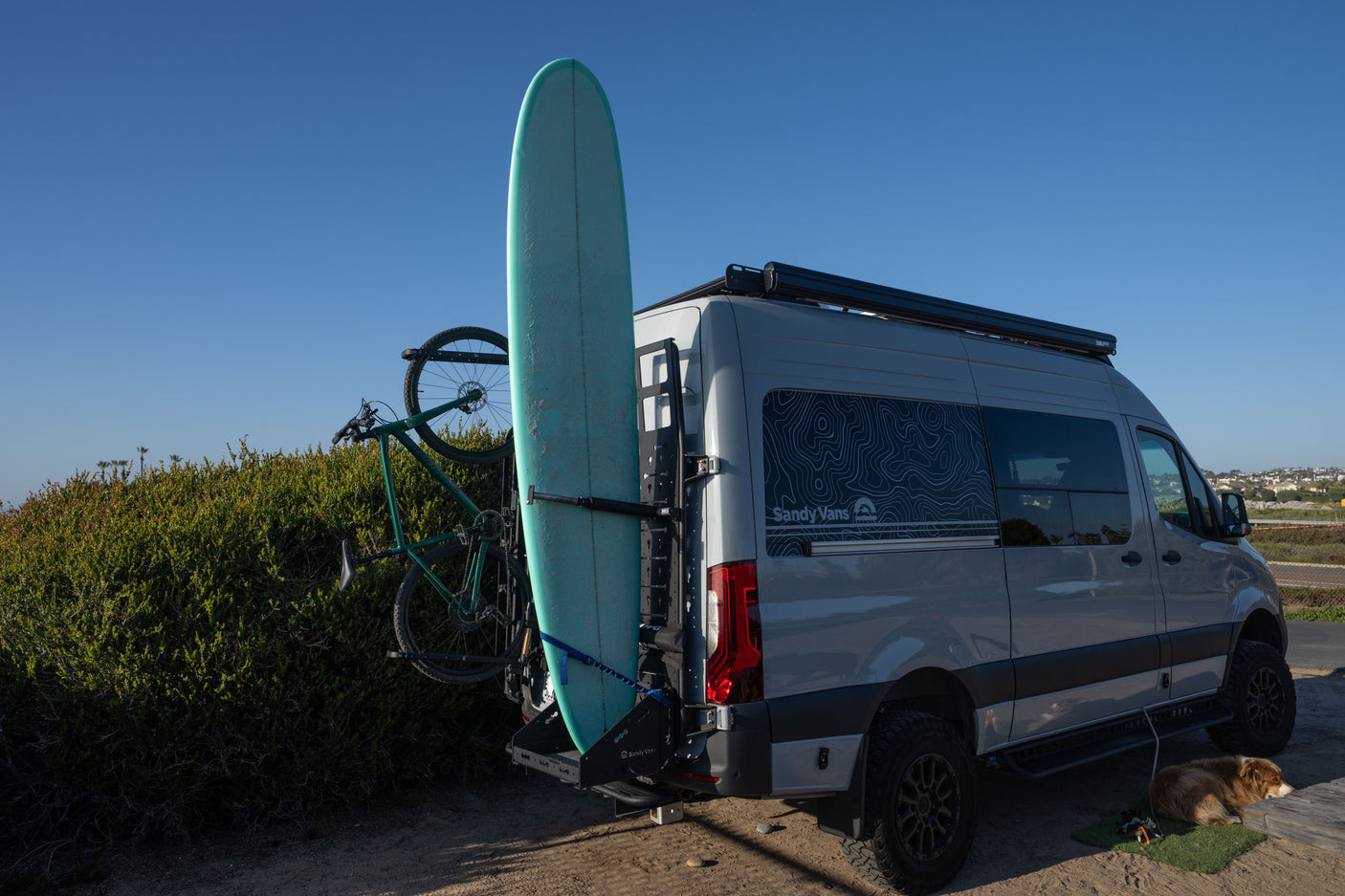 Adventure-ready RV rental van with surfboard, bike, and a sleepy dog. Perfect for outdoor travel and van life!
