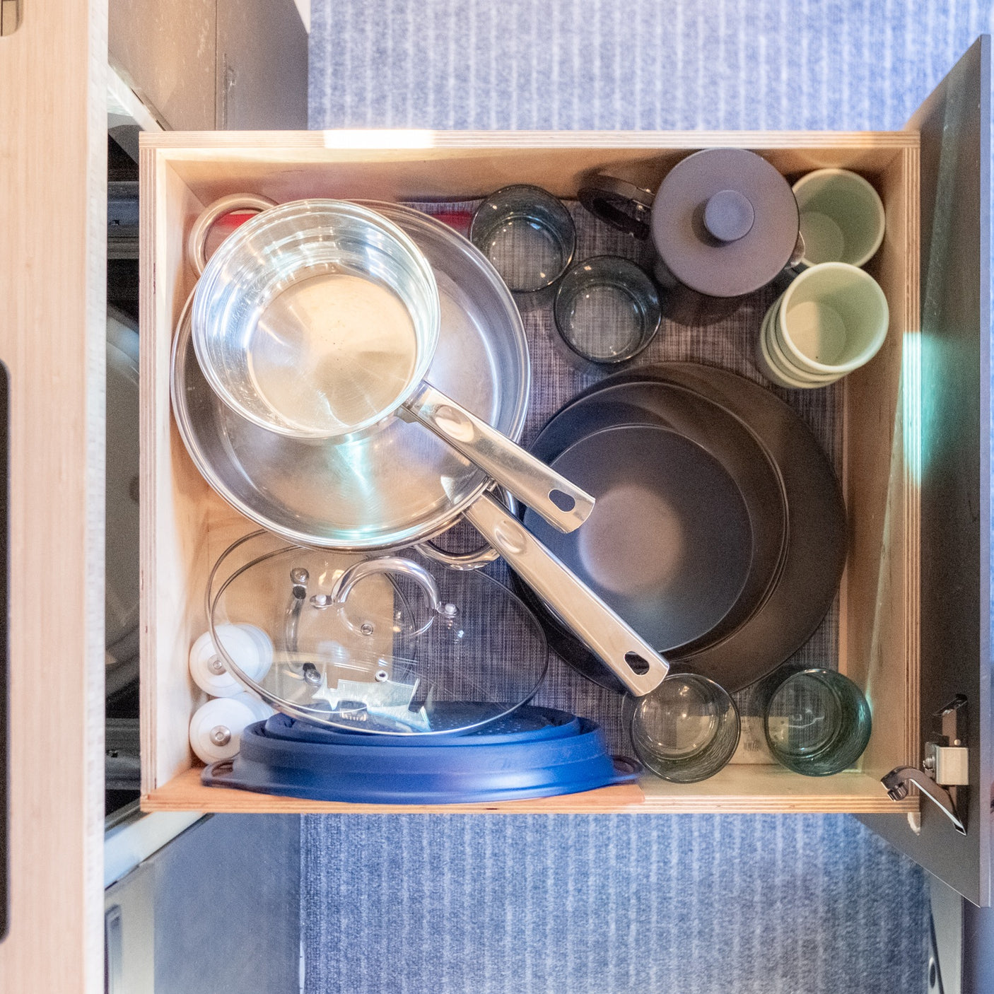 An RV rental's well-organized kitchen drawer holds stacked pots, pans, glasses, and a teapot for compact living.