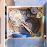 An RV rental's well-organized kitchen drawer holds stacked pots, pans, glasses, and a teapot for compact living.