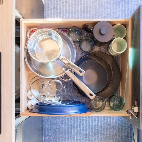 An RV rental's well-organized kitchen drawer holds stacked pots, pans, glasses, and a teapot for compact living.