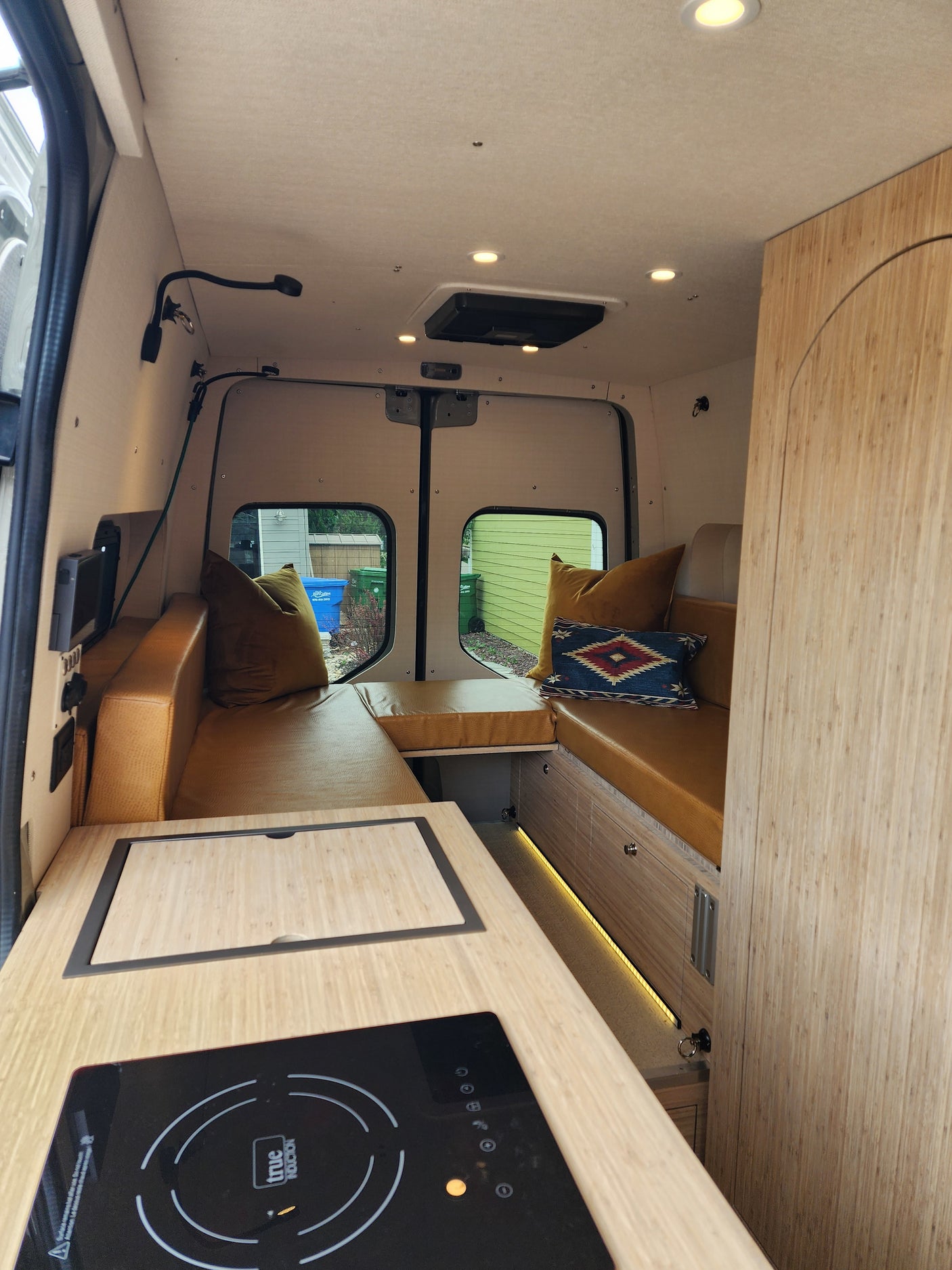 Modern RV rental interior: L-shaped lounge with leather cushions, kitchen counter, and induction cooktop for cozy adventures.