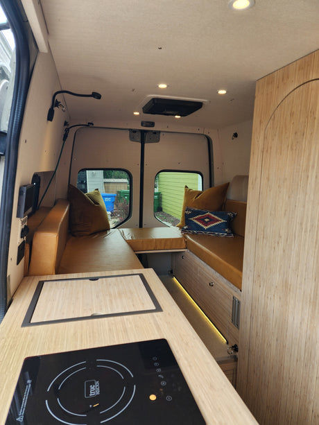 Modern RV rental interior: L-shaped lounge with leather cushions, kitchen counter, and induction cooktop for cozy adventures.