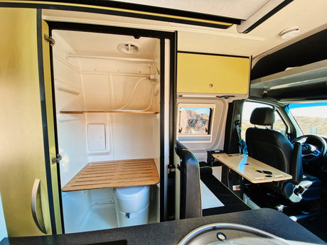 Compact RV rental interior featuring a shower/toilet, kitchen sink, driver's cabin, and scenic window view.