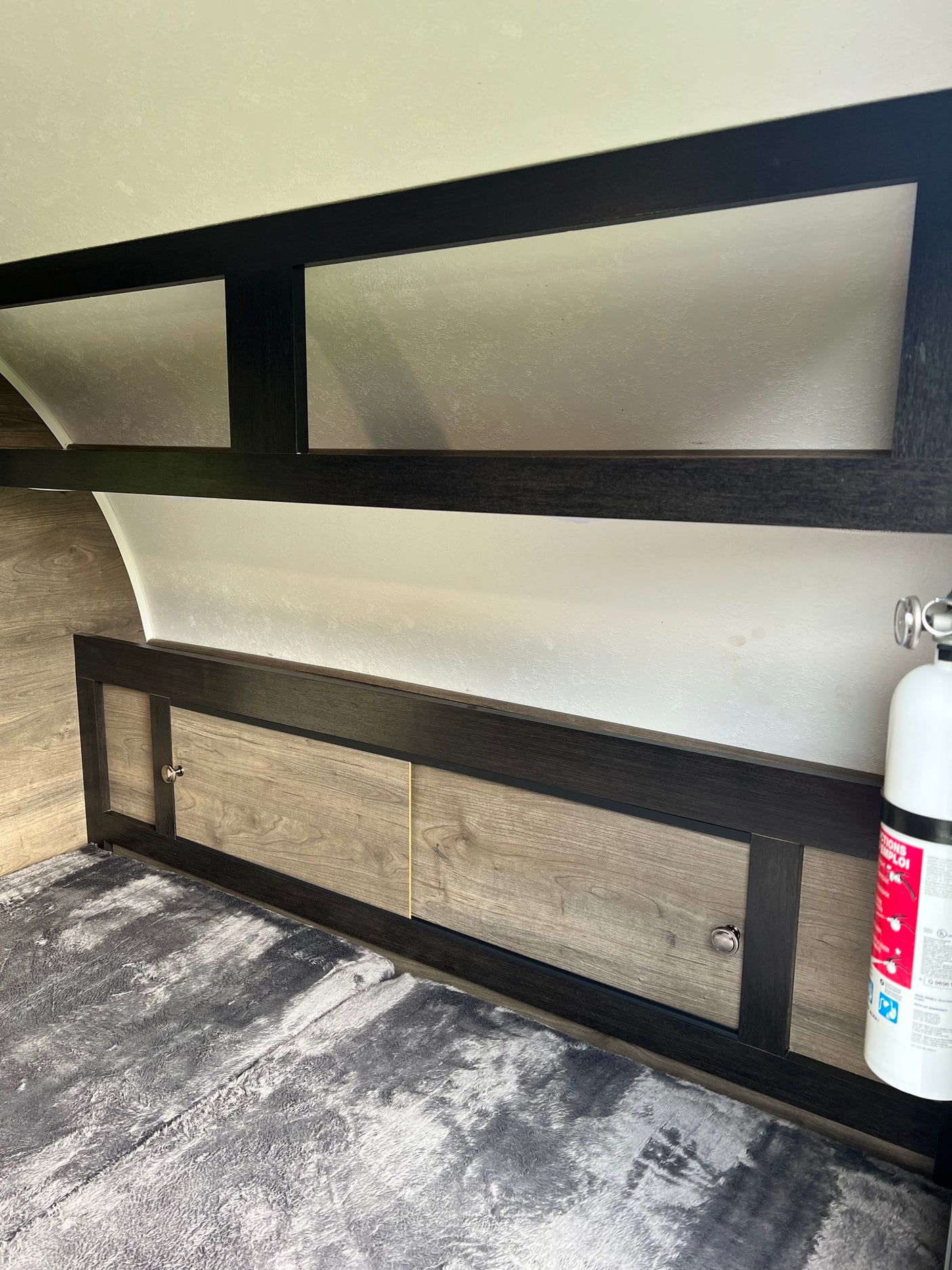 Spacious RV rental interior featuring a cozy bed, ample overhead storage, and an essential fire extinguisher for safe travels.
