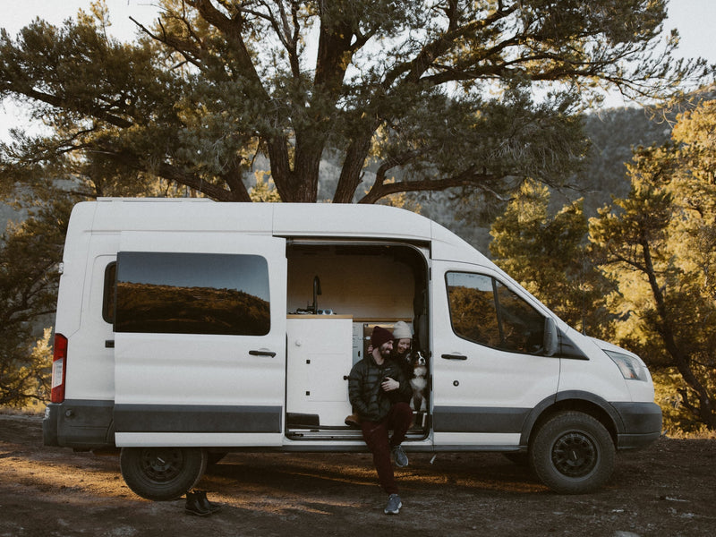  stepping out of their RV rental camper van for an adventure.|A happy couple and their dog relax in a white camper van with the door open — photo 2