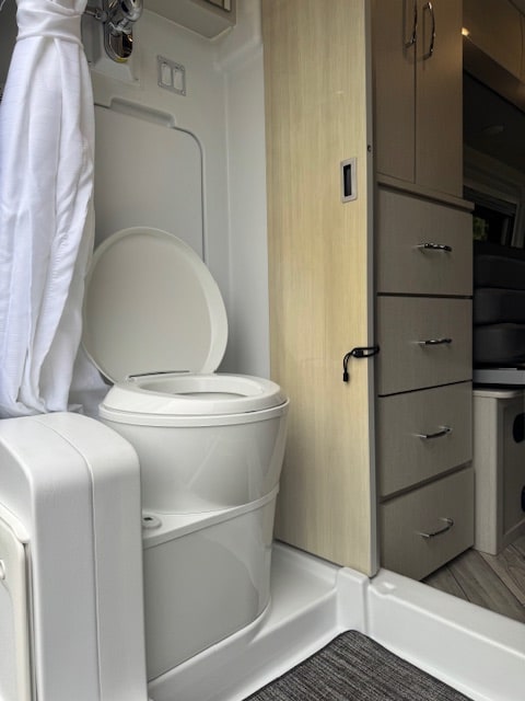 RV rental bathroom: A compact space with a white composting toilet, shower curtain, and integrated storage units.