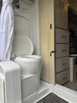 RV rental bathroom: A compact space with a white composting toilet, shower curtain, and integrated storage units.