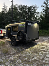 This sleek grey CORE RV rental, lit up for night, is hitched to a Tundra, set for rugged camping adventures in the forest.