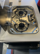 RV rental: A stainless steel, two-burner RV stove with its protective lid open, revealing black grates and control knobs.
