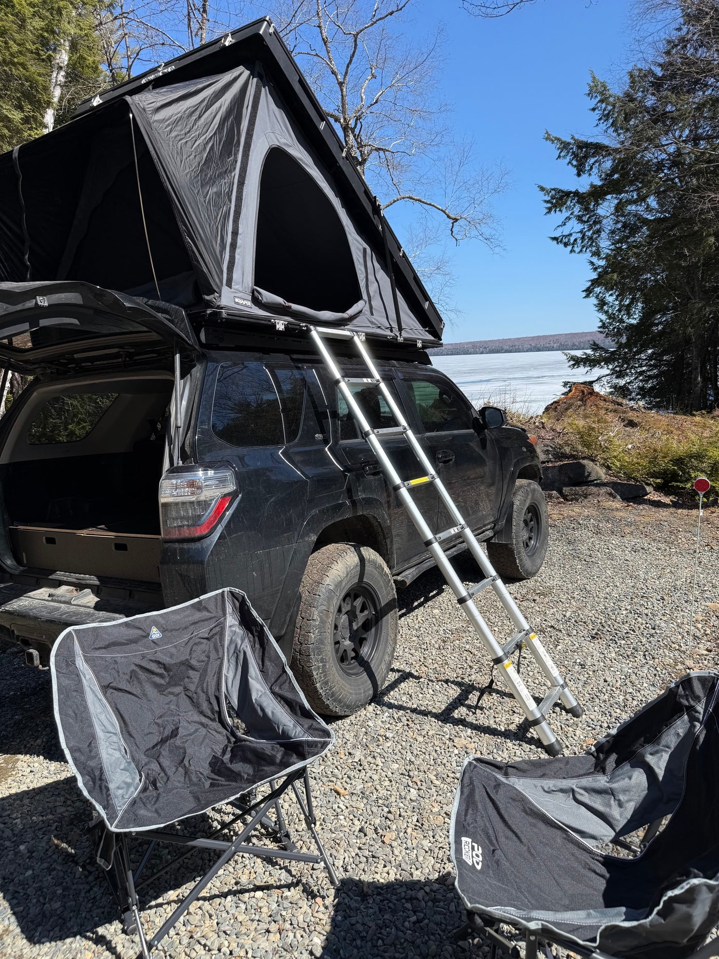Black SUV with a deployed roof top tent by a frozen lake, ideal for an RV rental camping getaway in nature.
