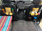 Inside an **RV rental**: front seats feature organized storage for travel gear, with a striped bed & clean floor.