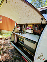 Ready for adventure! This T@G teardrop camper rv rental's outdoor kitchen features a stove, sink, fridge, and starry ceiling.