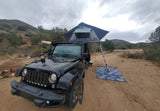 Black Jeep with a deployed rooftop tent & ladder, ready for off-road camping. Explore nature with this unique RV rental setup.
