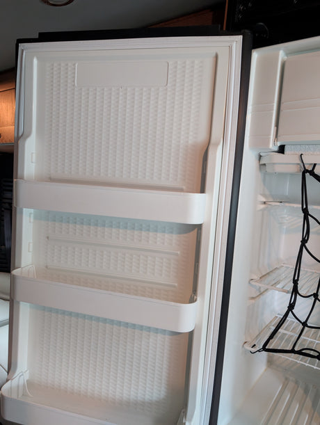 A compact rv rental refrigerator with an open door, showcasing door shelves and main compartment with a cargo net.