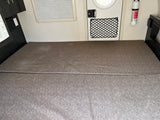 RV rental interior: a gray modular bed, adjacent cabinets, door with storage net, and fire extinguisher.