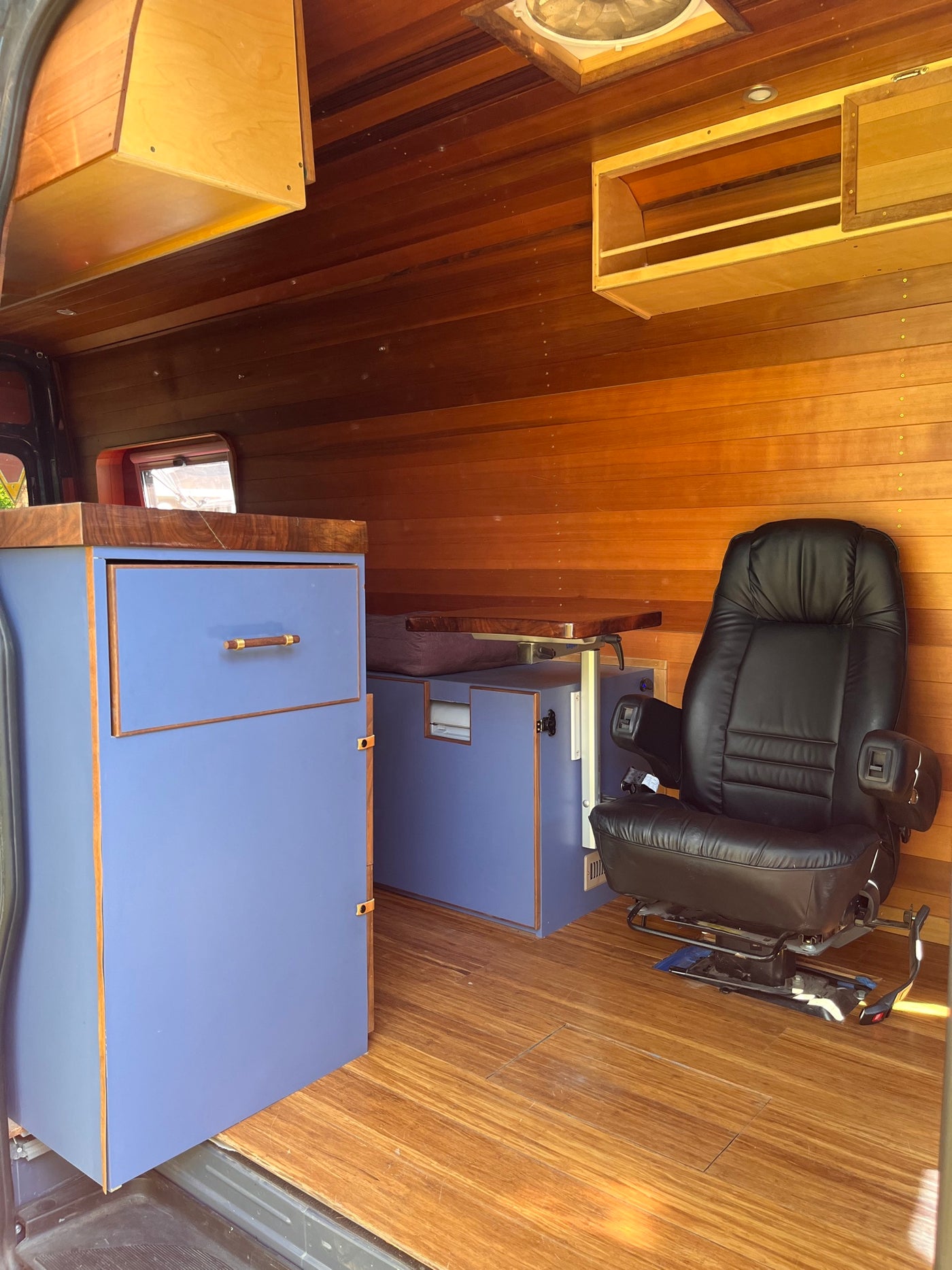 RV rental: Inside a custom wood-paneled RV, featuring a black leather office chair, blue cabinets, and a mobile workspace. — photo 12