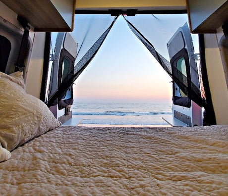 Inside an rv rental, a cozy bed offers a breathtaking ocean view from an open van. Perfect for travel & camping.