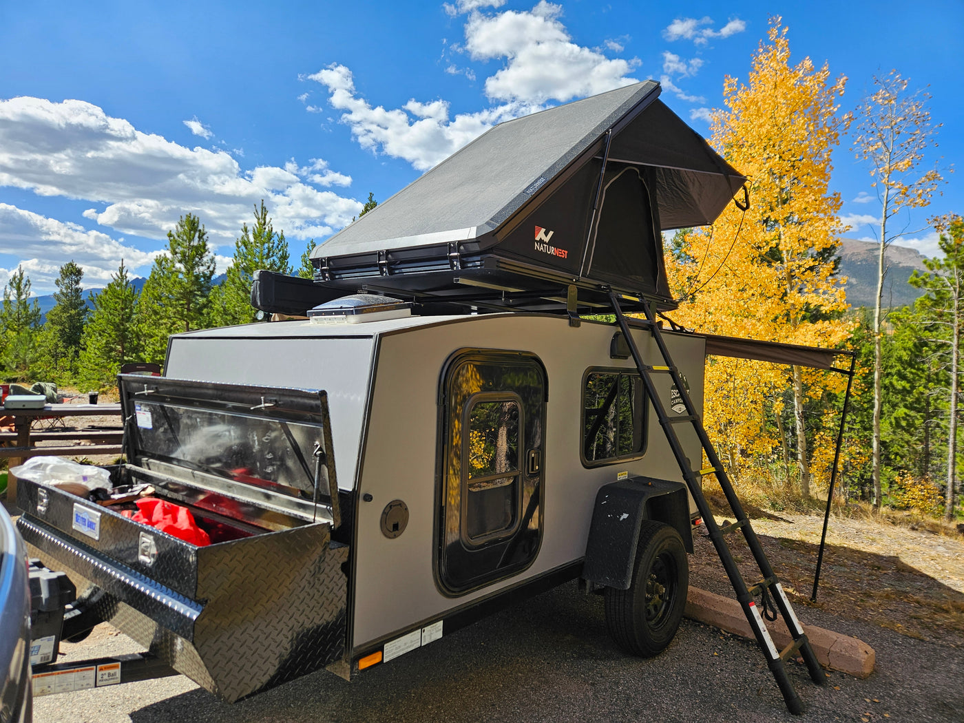Teardrop camper trailer with a NaturNest rooftop tent, parked in a scenic fall mountain setting, great for an RV rental.