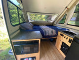 Cozy RV rental interior: bed, compact kitchenette, and large windows overlooking nature. Ideal for serene getaways.