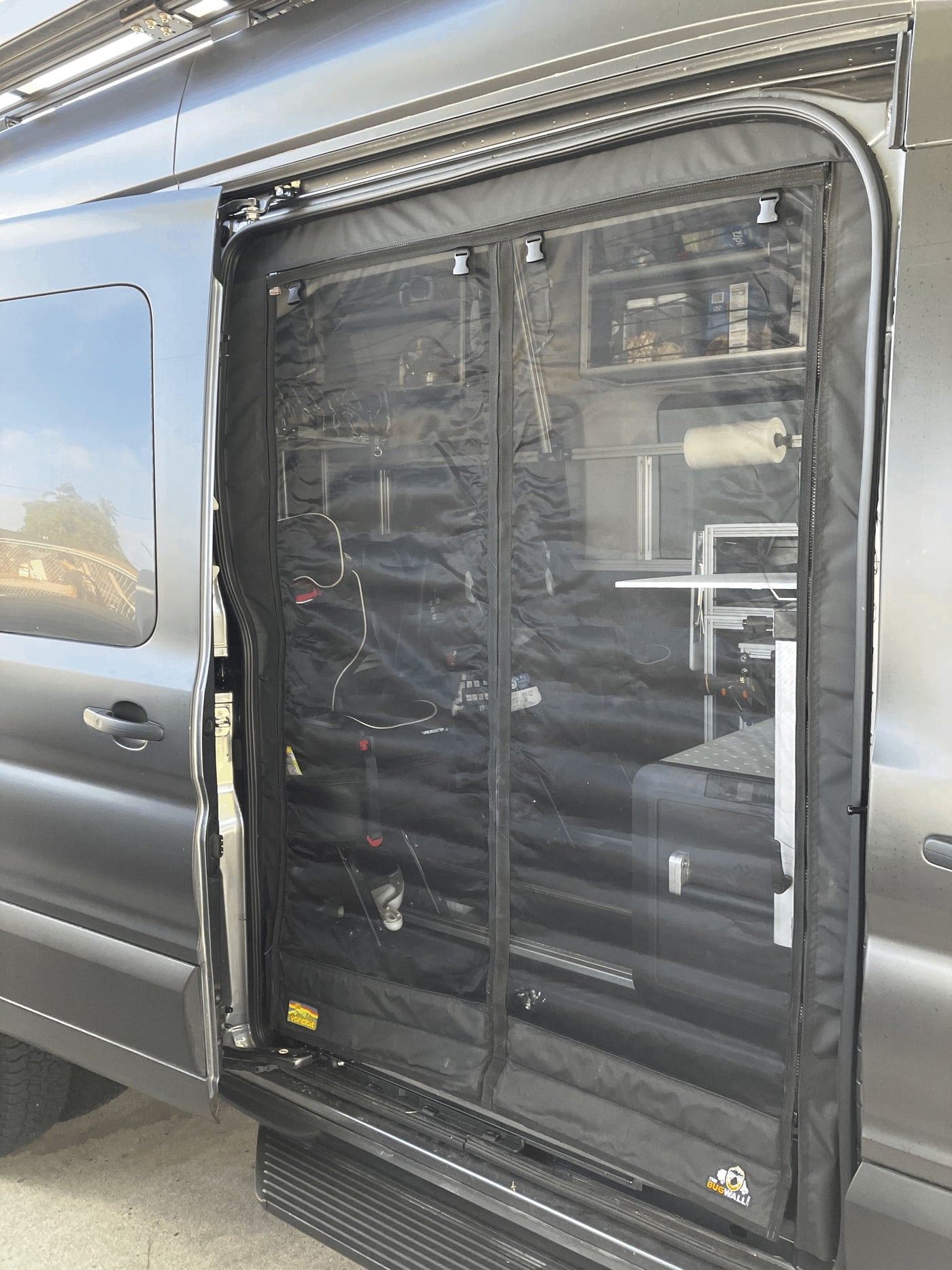 RV rental ready: gray van's side door open, revealing a black mesh bug screen. Organized interior shelves & gear visible for trips. — photo 12