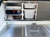 RV rental compact kitchen: organized cabinets with dishes, storage bins, stainless sink, and countertop, ready for travel.