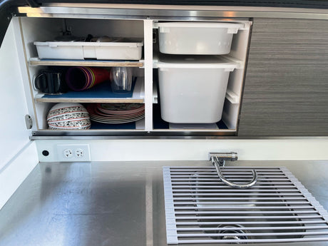 RV rental compact kitchen: organized cabinets with dishes, storage bins, stainless sink, and countertop, ready for travel.