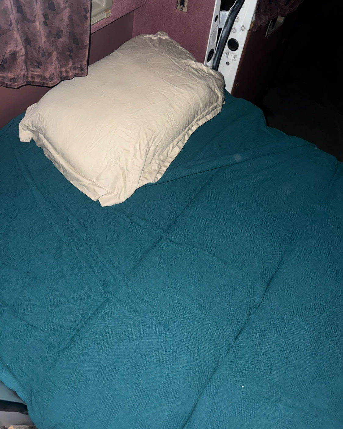 RV rental interior: A beige pillow rests on a teal blanket-covered bed, nestled against dark red walls.