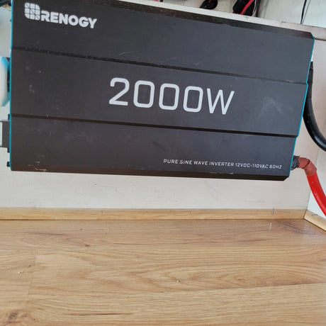A black Renogy 2000W Pure Sine Wave Inverter, essential for off-grid power in an RV rental setup.