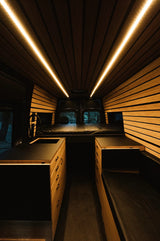 Cozy RV rental interior with wooden slatted ceilings, warm LED lights, and built-in bed, kitchen, and storage.