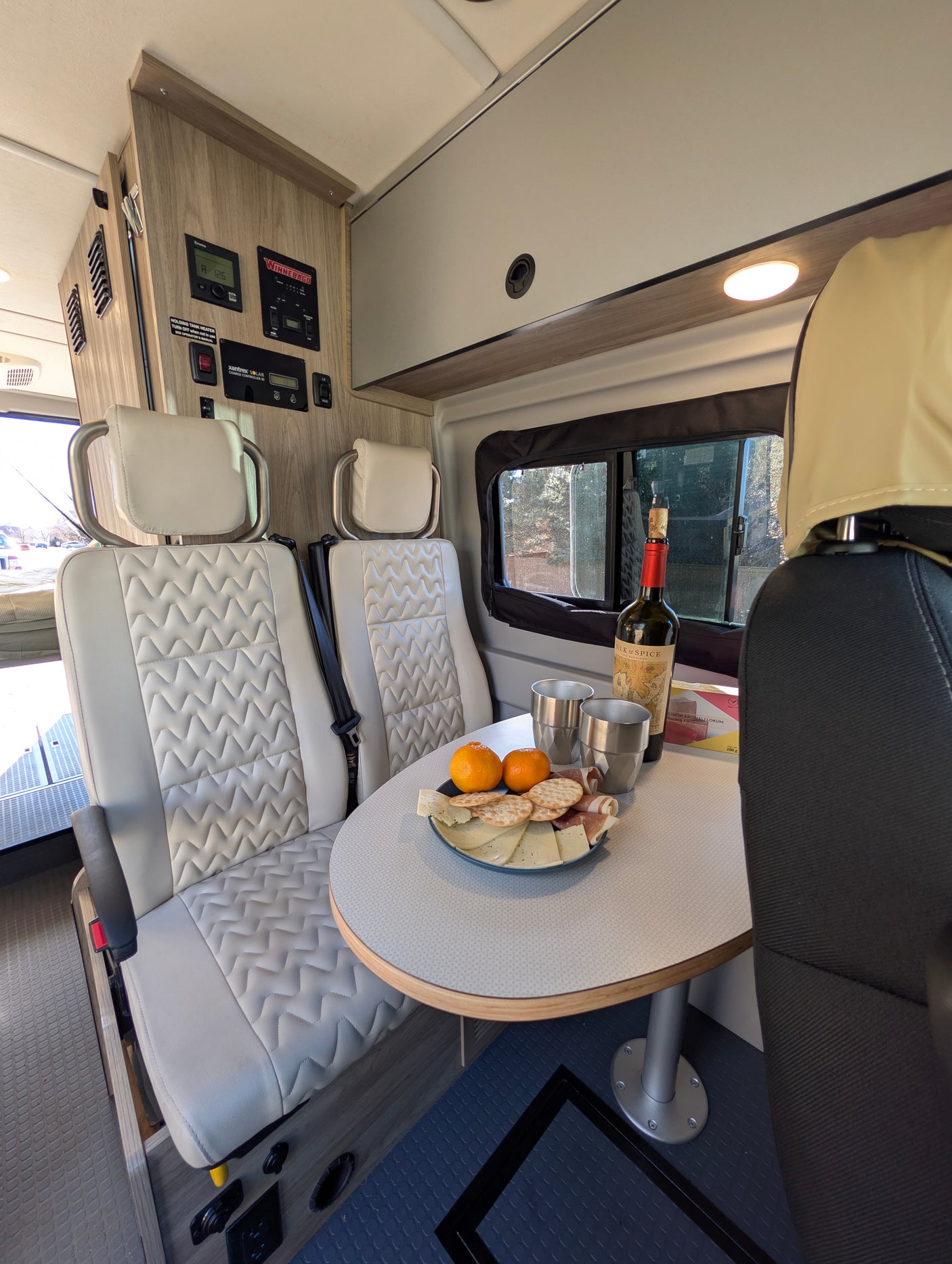 Winnebago rv rental dining area features charcuterie, wine, comfortable seating, and control panel.